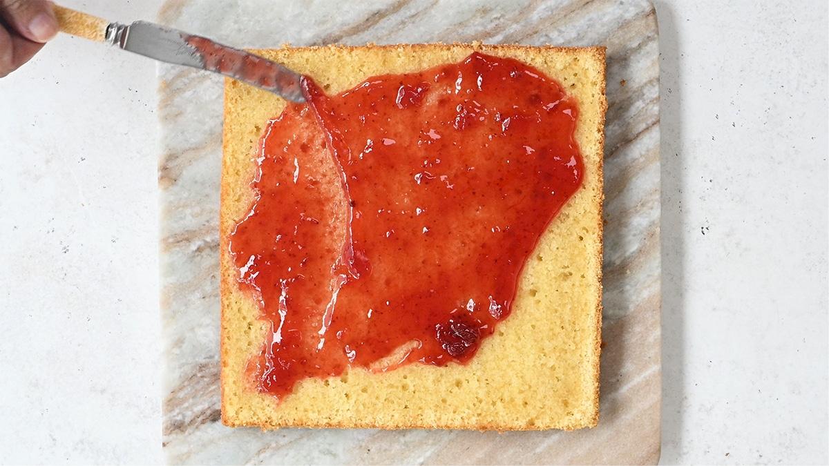 spreading Victoria sponge cake with strawberry jam