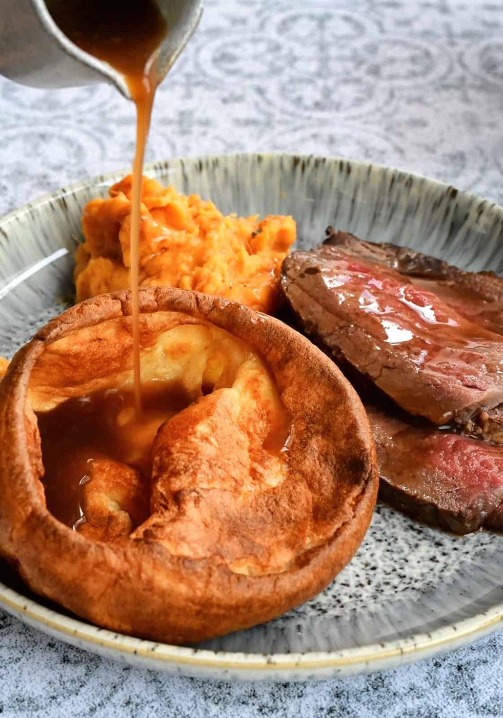 Gravy being poured over large Yorkshire pudding