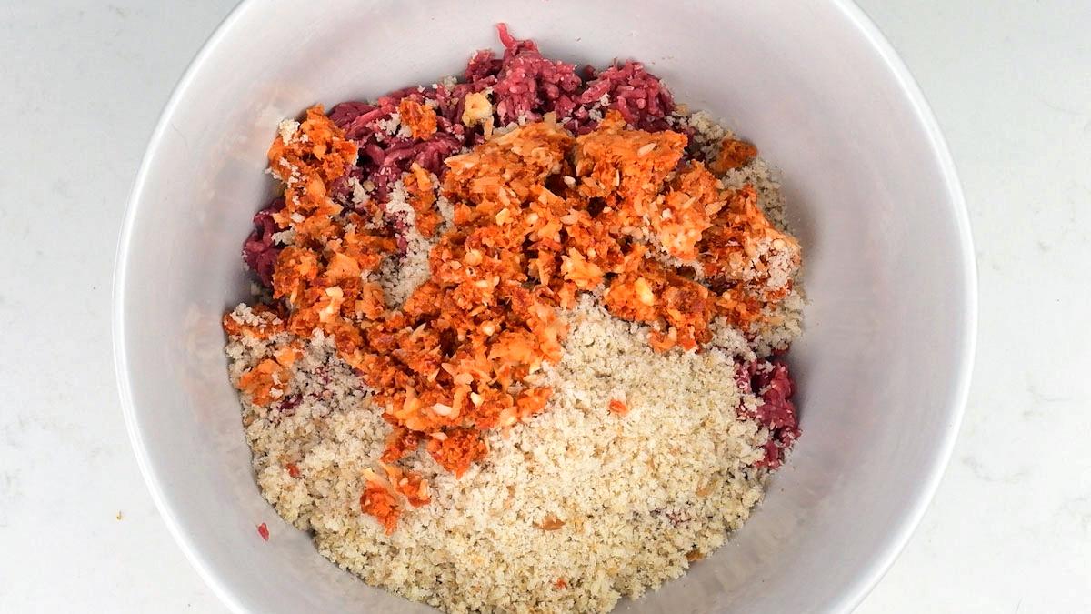 A white bowl containing ground meat, breadcrumbs, and a mixture of finely chopped vegetables or seasonings, ready to be mixed together for delicious Spanish meatballs, also known as albondigas.