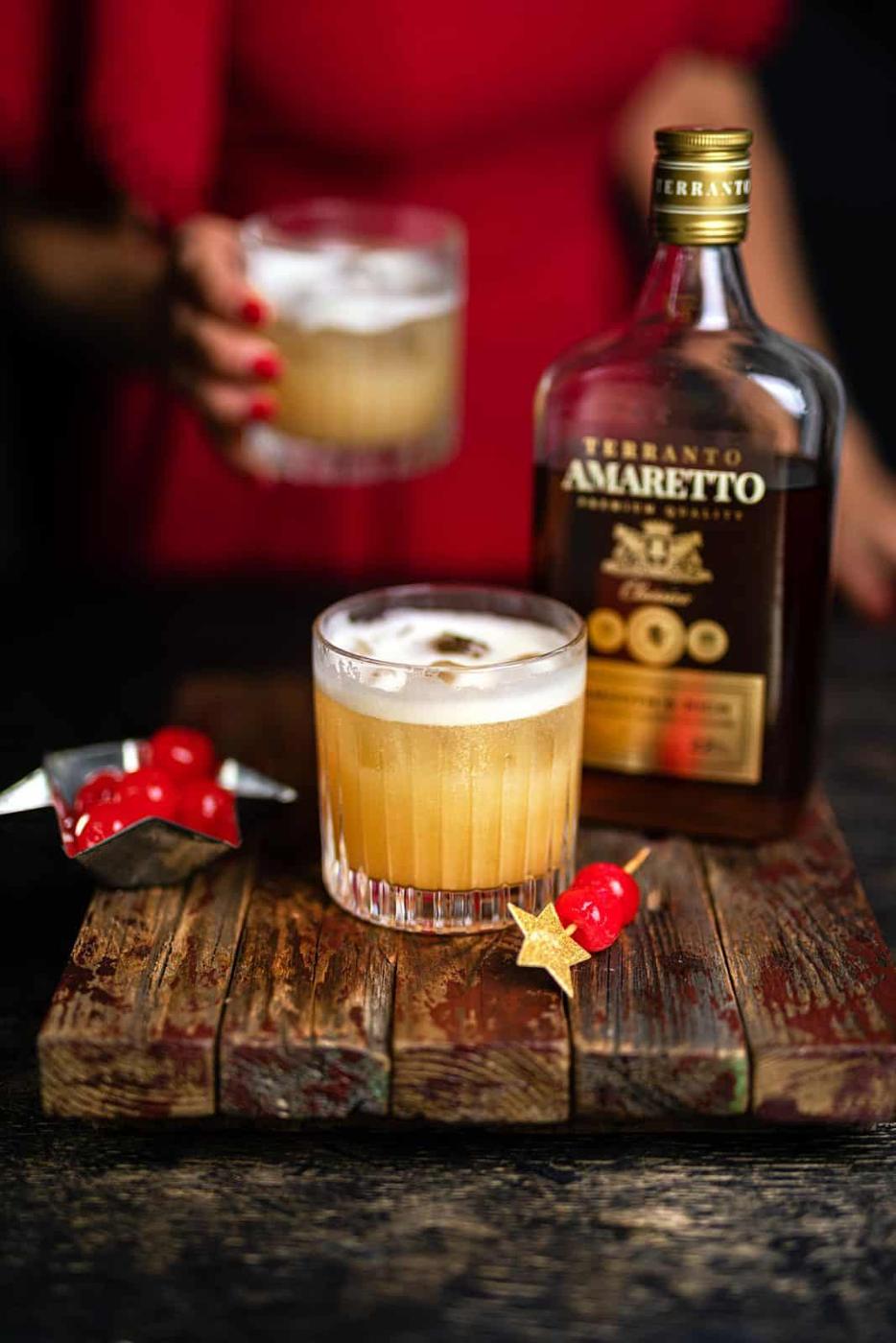 Old fashioned glass with amaretto sour cocktail on the rocks and cocktail cherries on the side