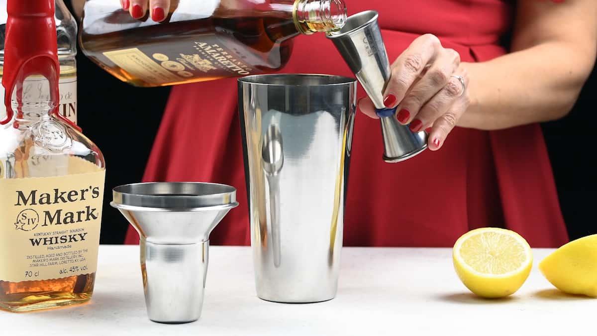 Measuring Amaretto liqueur in a jigger to add to cocktail shaker