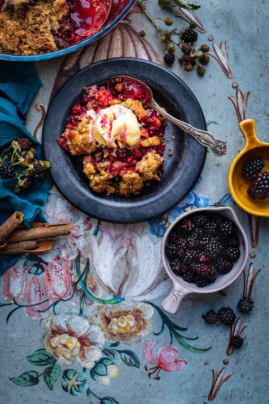 Bowl of apple and blackberry crumble served with ice cream, overhead view