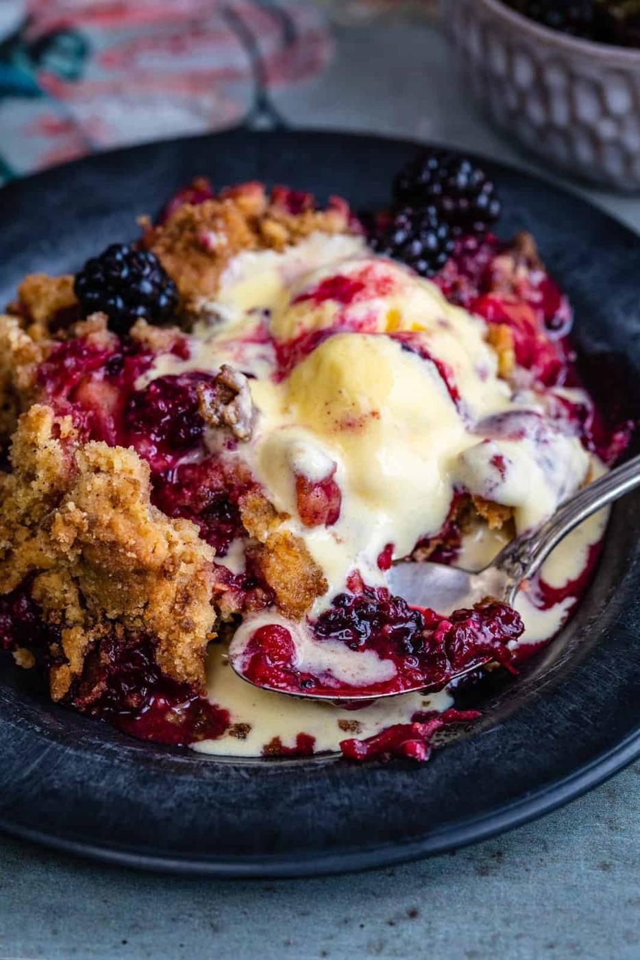 close up on a bowl of apple and black berry crumble topped with vanilla ice cream