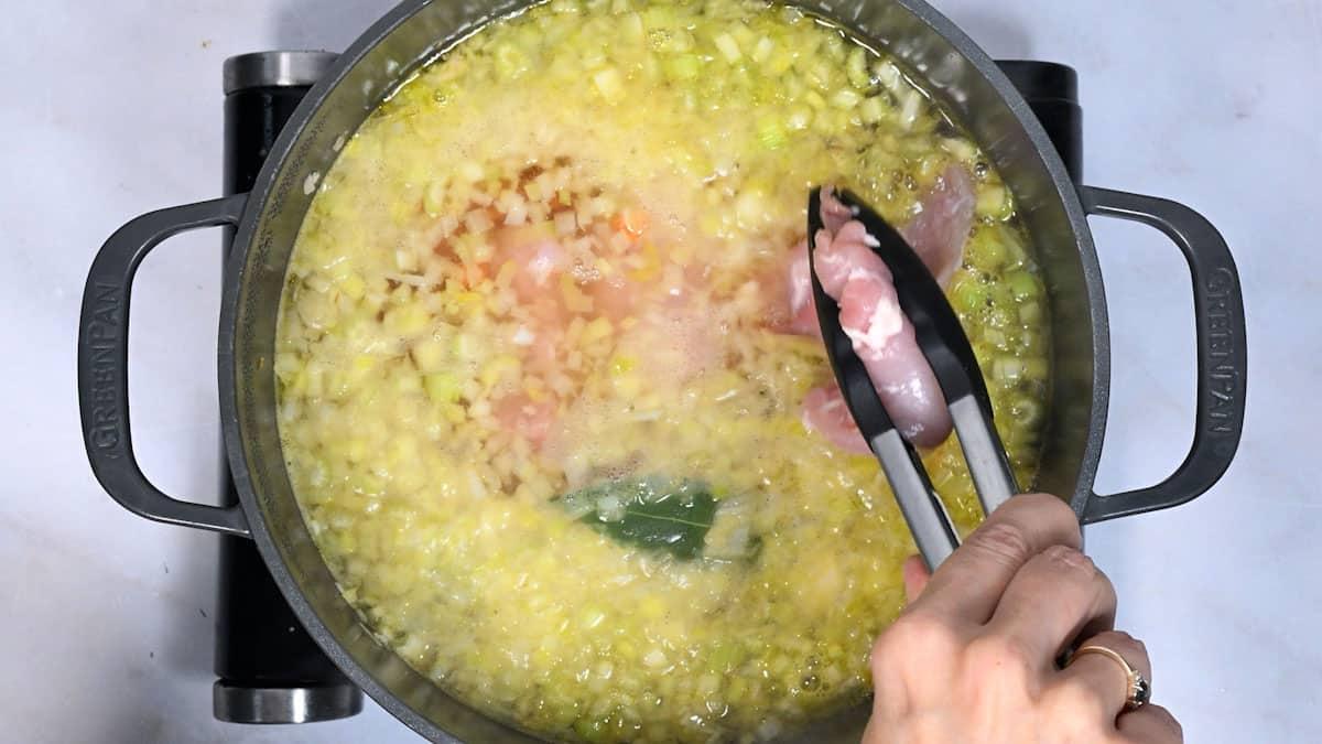 adding chicken to a pot of simmering broth