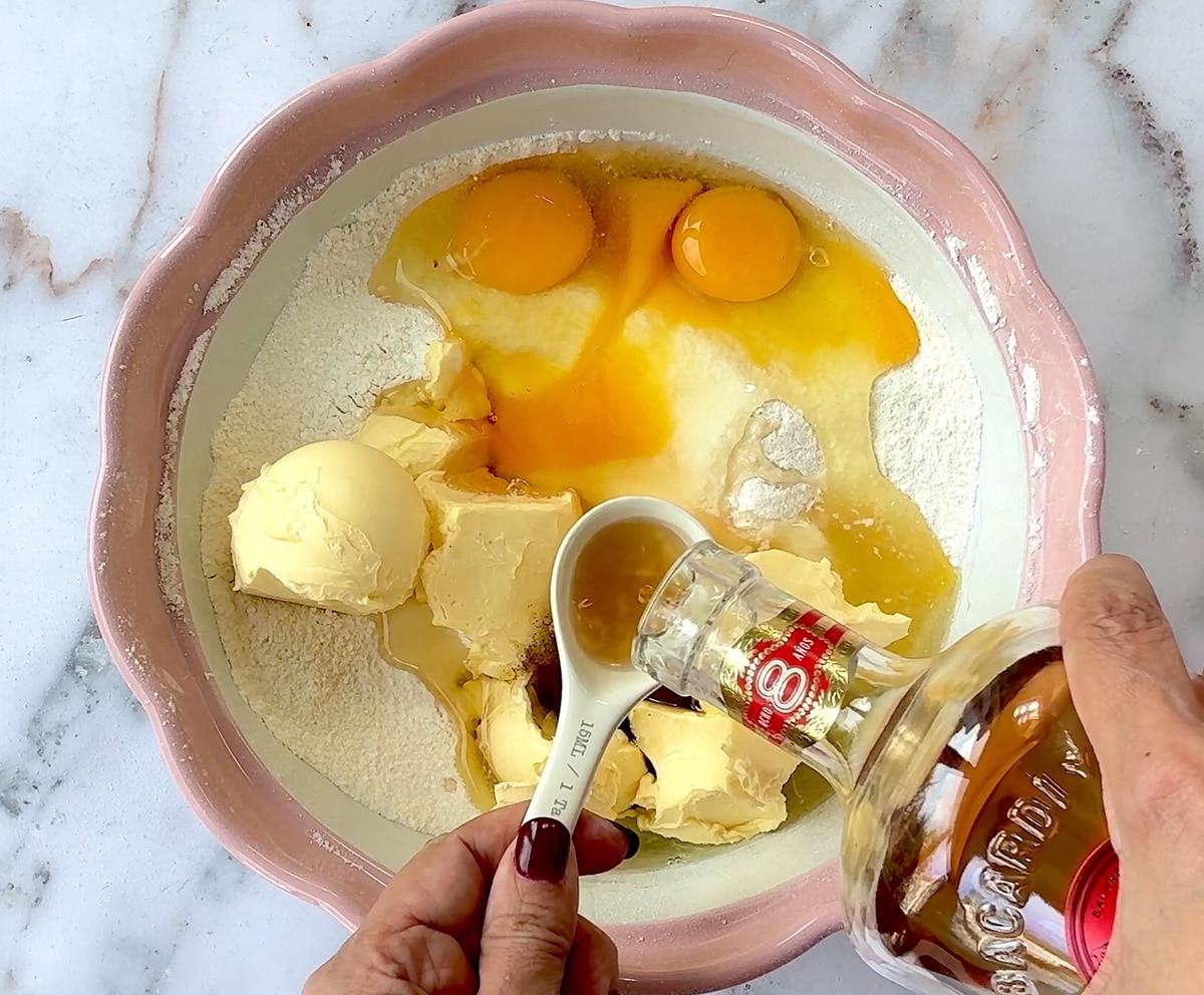 ingredients for um cake in a mixing bowl, rum being added