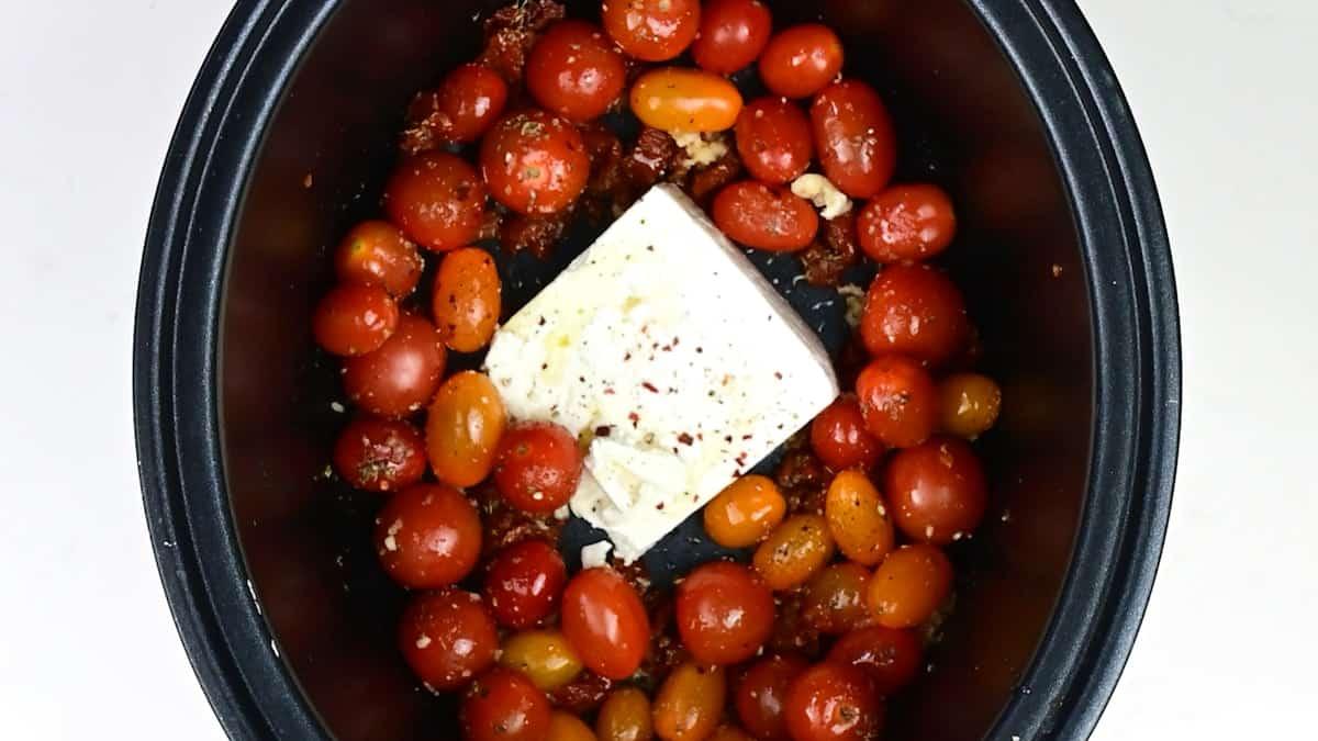 Cherry tomatoes with garlic, herbs and seasoning and block of feta cheese in a slow cooker