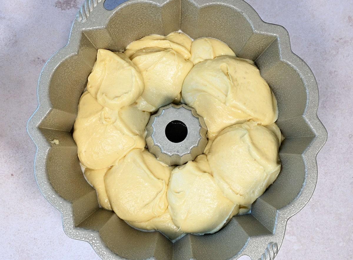 Top view of a bundt pan filled with smooth, creamy yellow cake batter, ready for baking. The batter is evenly distributed within the pans fluted design. The pan rests on a light-colored countertop.
