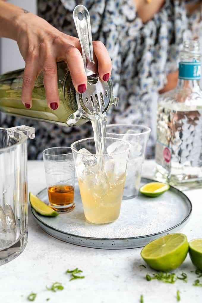 Cadillac Margarita being strained into a glass filled with ice with Grand Marnier on the side