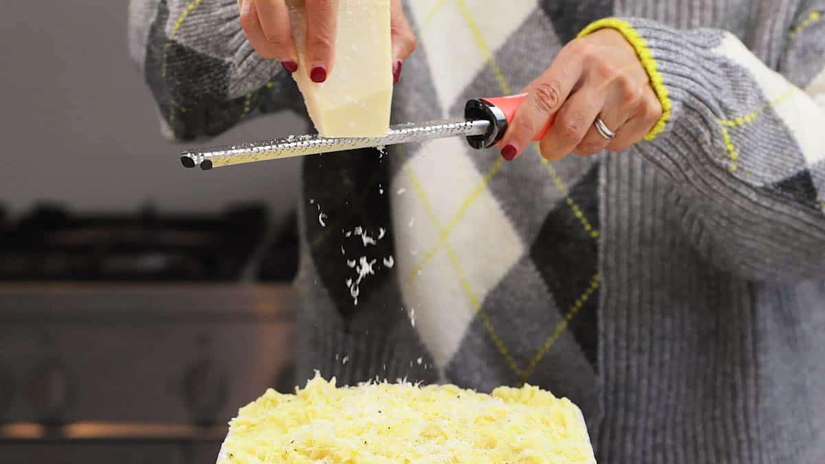 Cheese being grated over the mashed potato topping of a fish pie