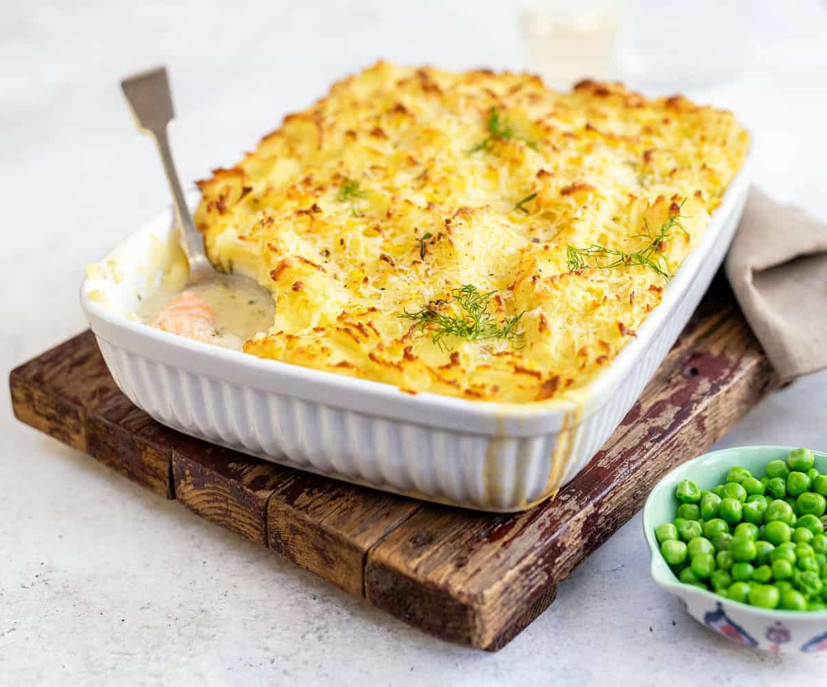 Baked fish pie with golden mashed potato topping in an ovenproof dish, served with peas