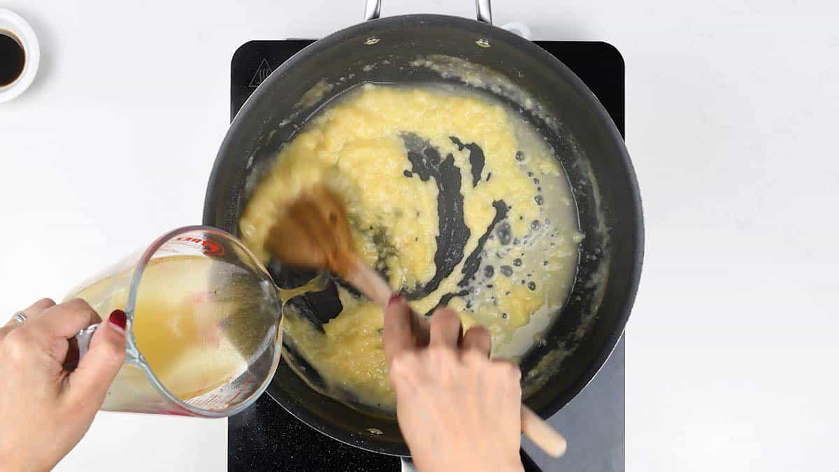 Fish stock being poured into the pan and stirred to make a smooth fish pie sauce