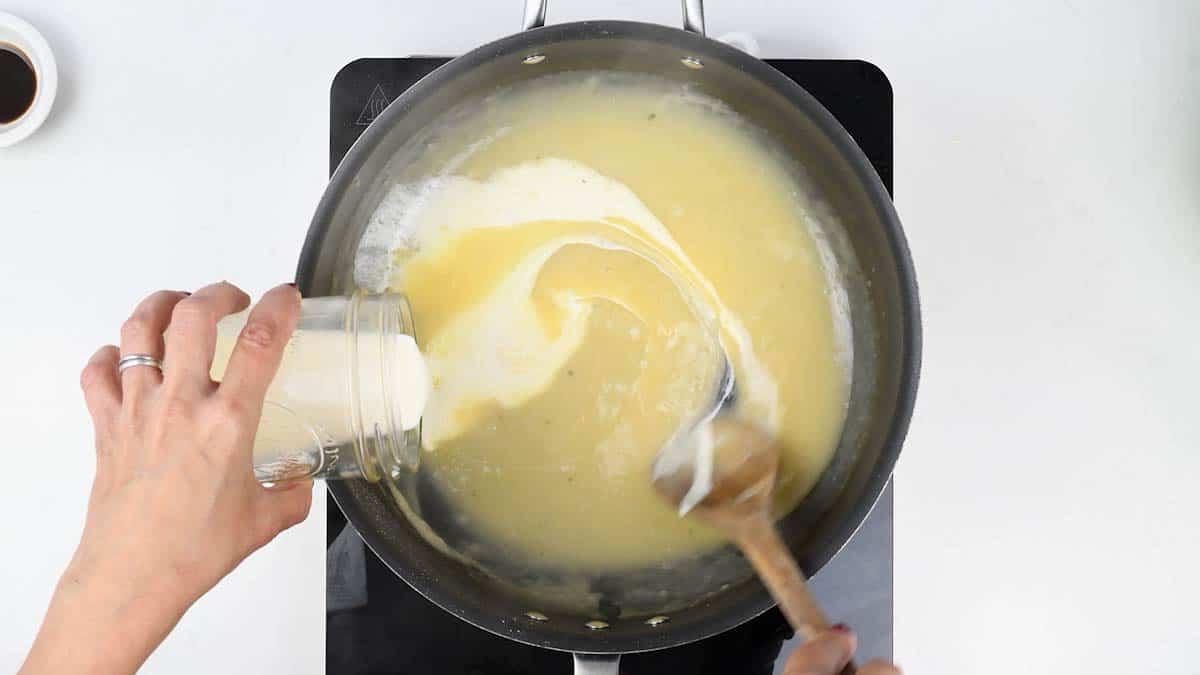 Cream being poured into the white wine sauce for fish pie