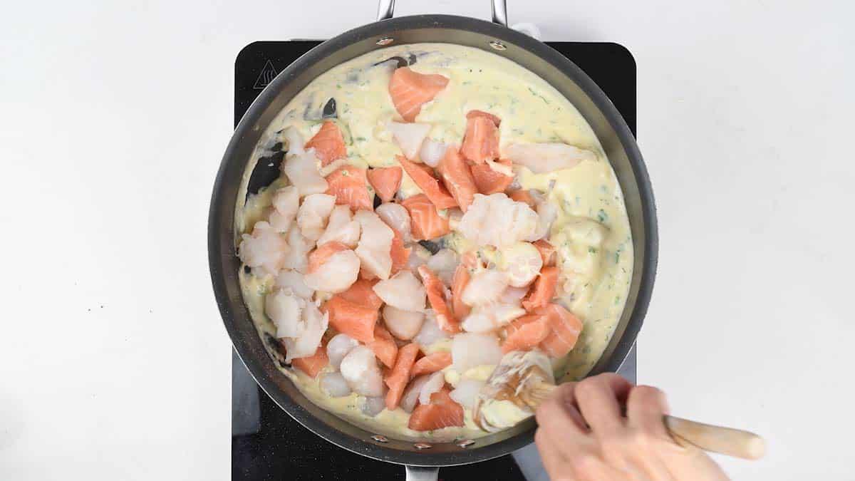Chunks of salmon, white fish and shrimp being folded into the creamy sauce