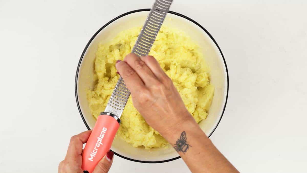 Nutmeg being grated over a bowl of buttery mashed potatoes