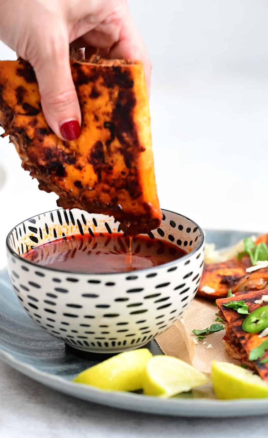 Dipping Birria taco into a bowl of sauce