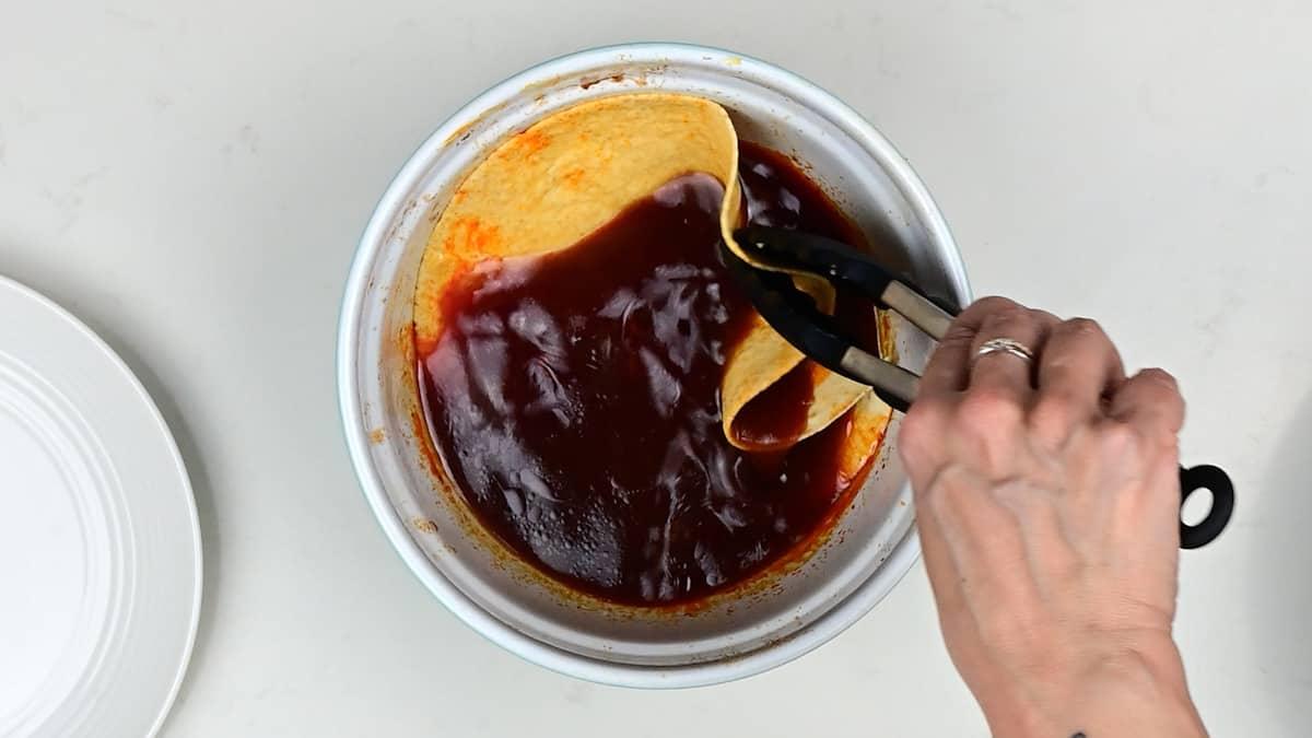 dipping a corn tortilla into birria taco sauce