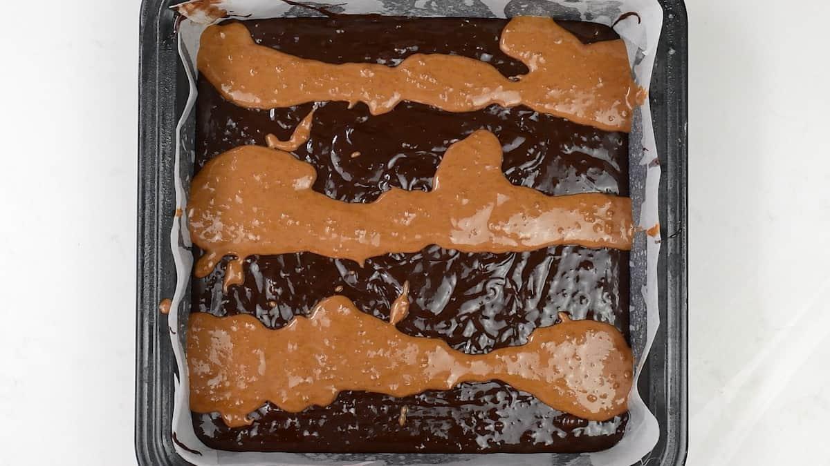 drizzling Biscoff spread over brownie batter in a square tin