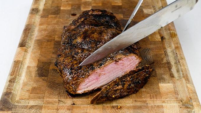 Slicing BBQ boneless leg of lamb on a wooden board