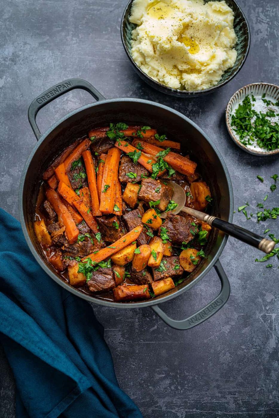 Pot of braised beef against a dark background with mashed potatoes on the side