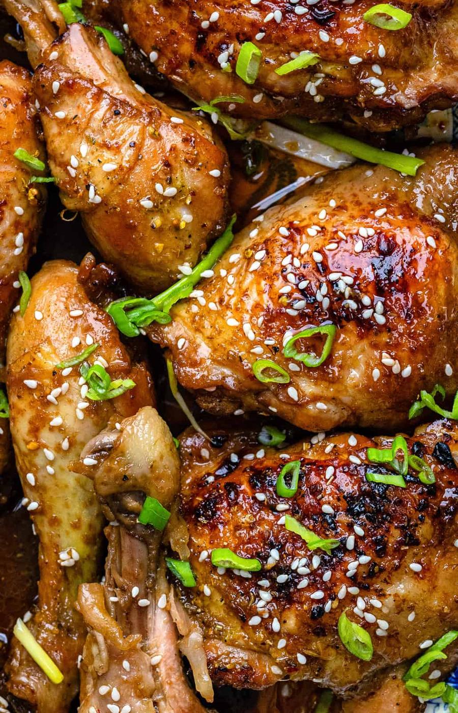 Close-up of golden-brown braised chicken thighs and drumsticks, cooked to perfection in a Dutch oven, then garnished with sesame seeds and sliced green onions. The chicken looks juicy and bursting with flavor.