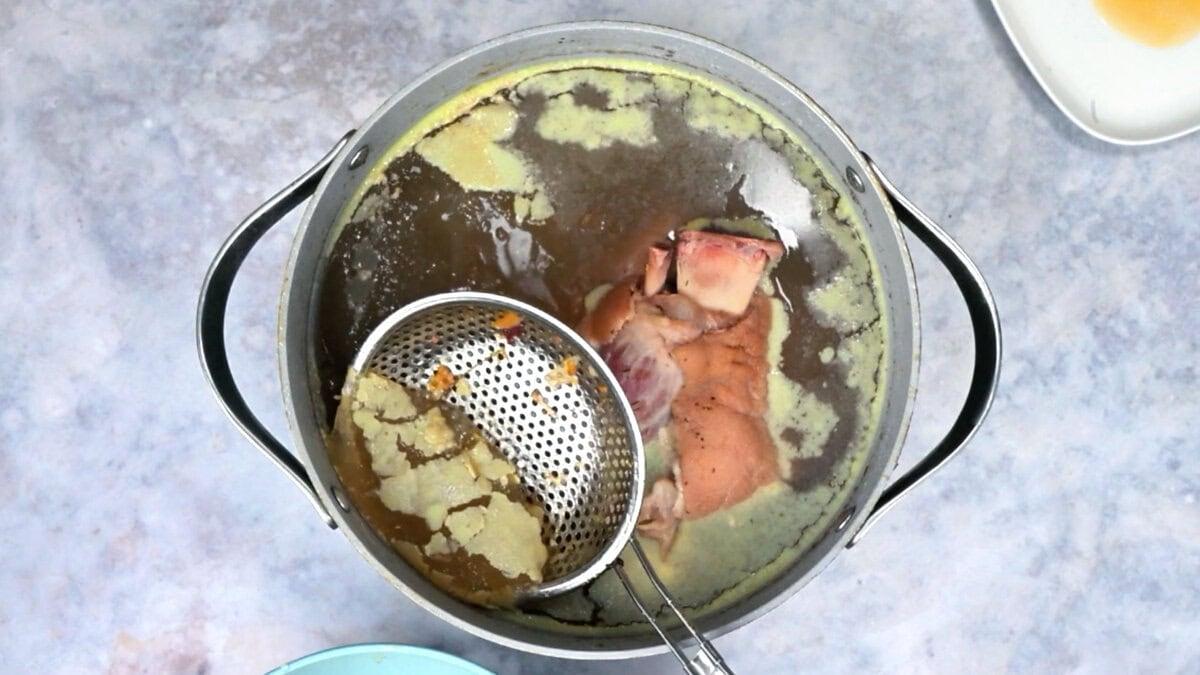 Skimming the ham hock braising liquid with a small mesh strainer before storing it as stock.