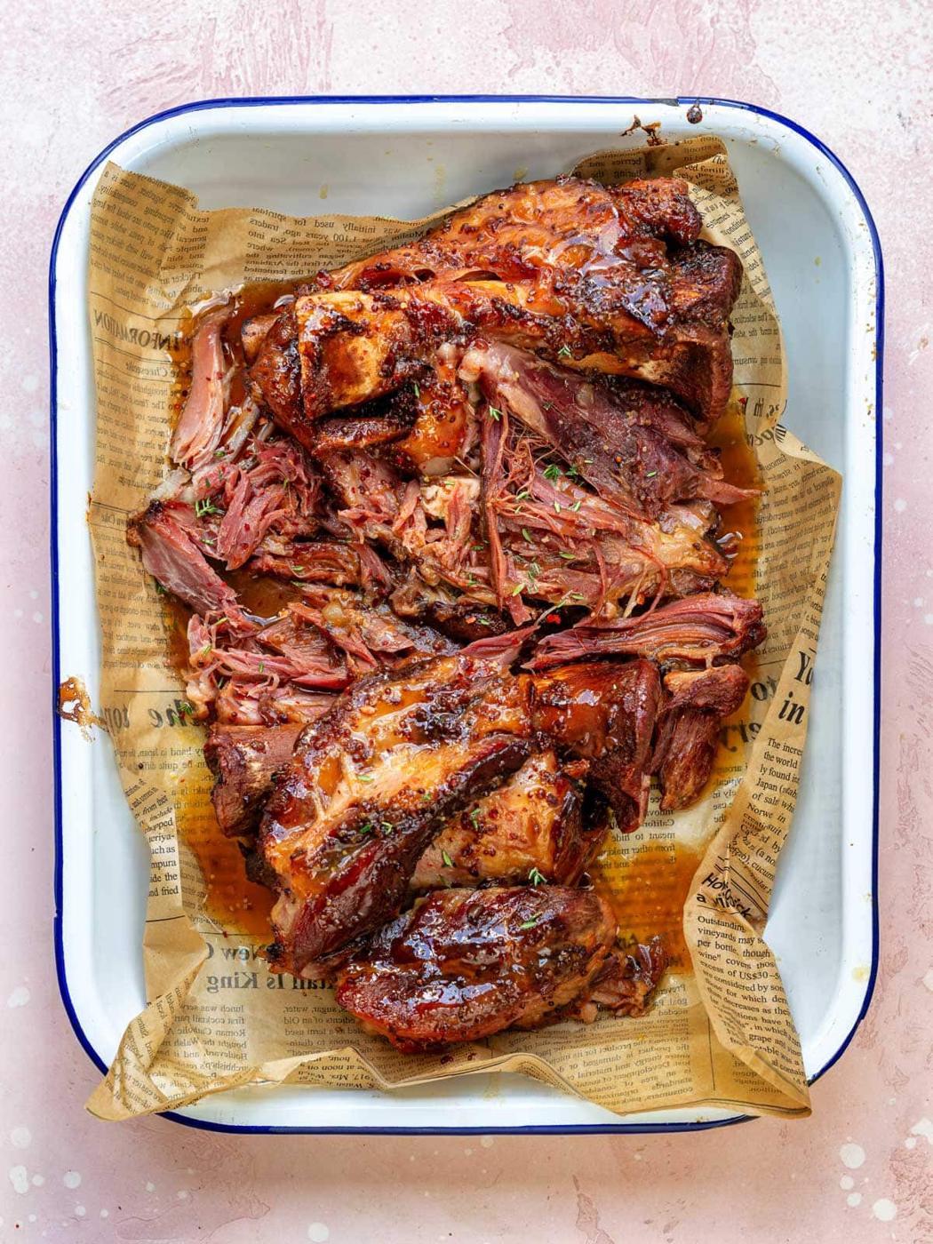 Braised ham hock with a sticky maple mustard glaze, pulled into tender pieces and served in a white enamel tray lined with paper.