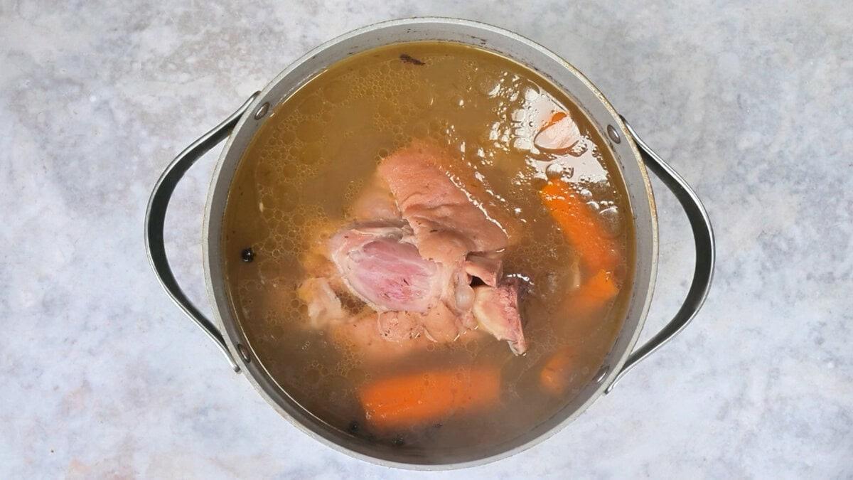 Braised ham hock in a pot of braising liquid with carrots, cooked until tender.