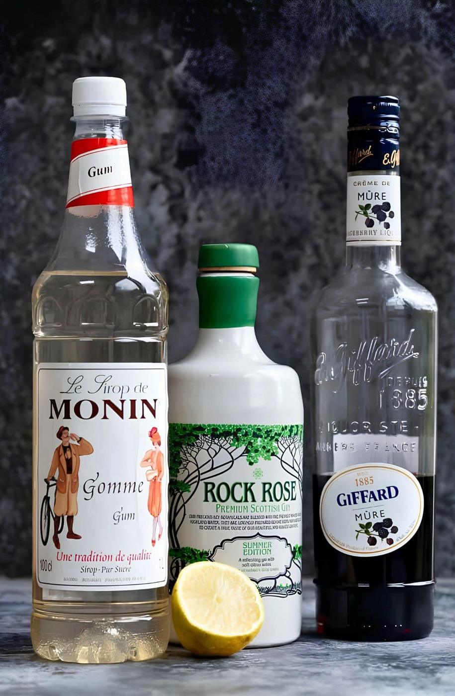 Bramble cocktail ingredients: bottles of Monin gomme syrup, Rock Rose gin and Giffard crème de mûre with half a lemon.