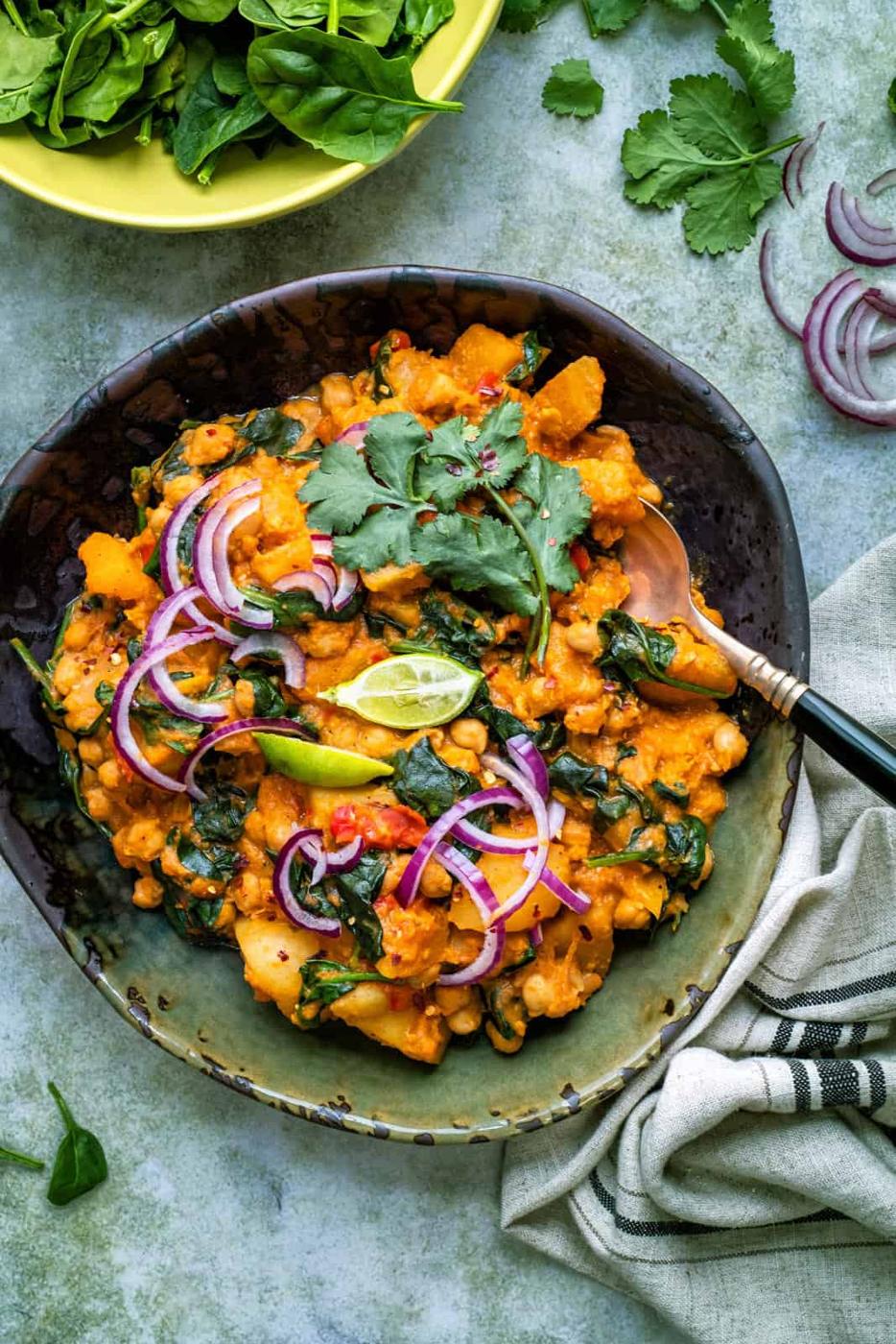 Butternut squash curry with chickpeas, coconut and spinach in a large bowl garnished with cilantro and lime