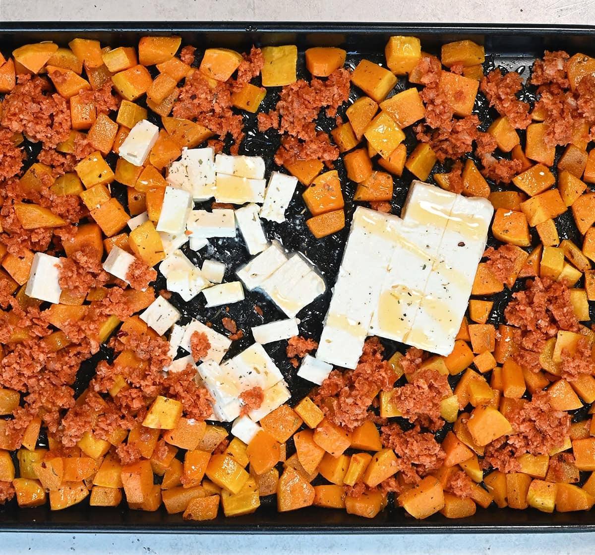 cubed butternut squash, crumbled chorizo and feta cheese on a tray