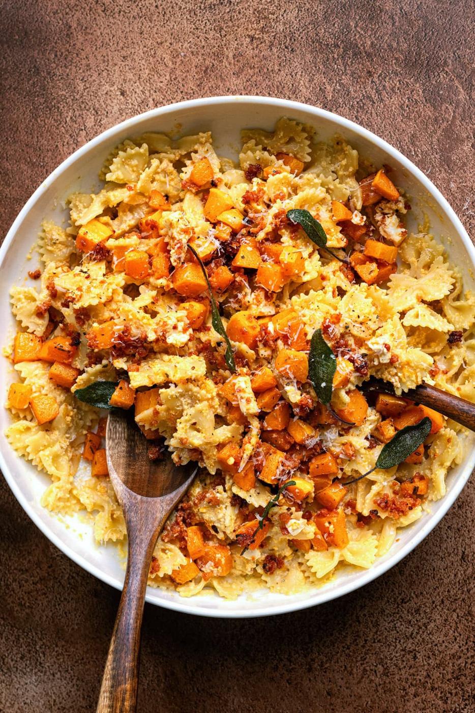 Baked feta, roasted butternut squash and chorizo pasta in a white bowl with two wooden spoons