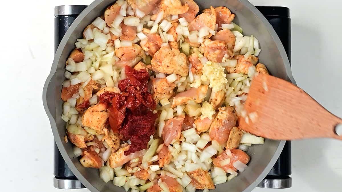 Chicken, onion, tomato paste and sundried tomatoes cooking in a pan
