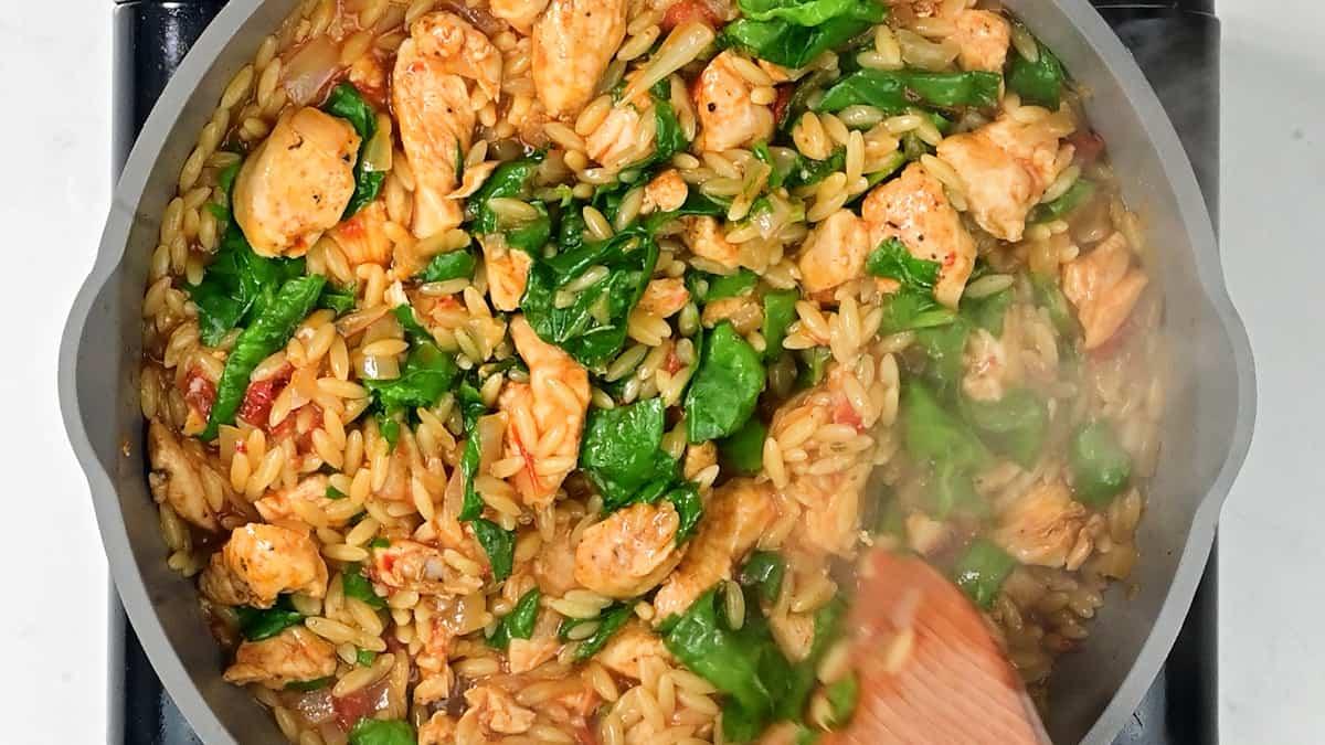 stirring spinach into chicken and orzo