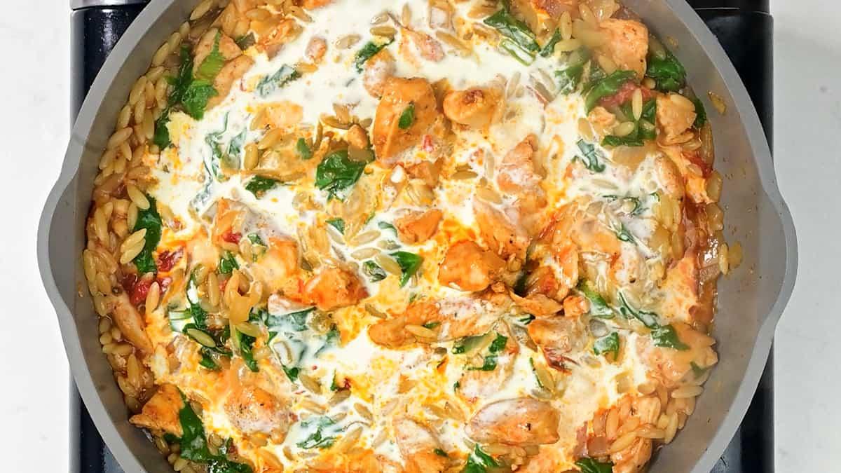 stirring cream into cajun chicken orzo in a pan