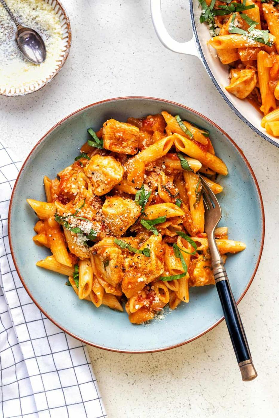 blue bowl with a serving of Cajun Chicken Pasta, fork on the side, casserole dish visible top right