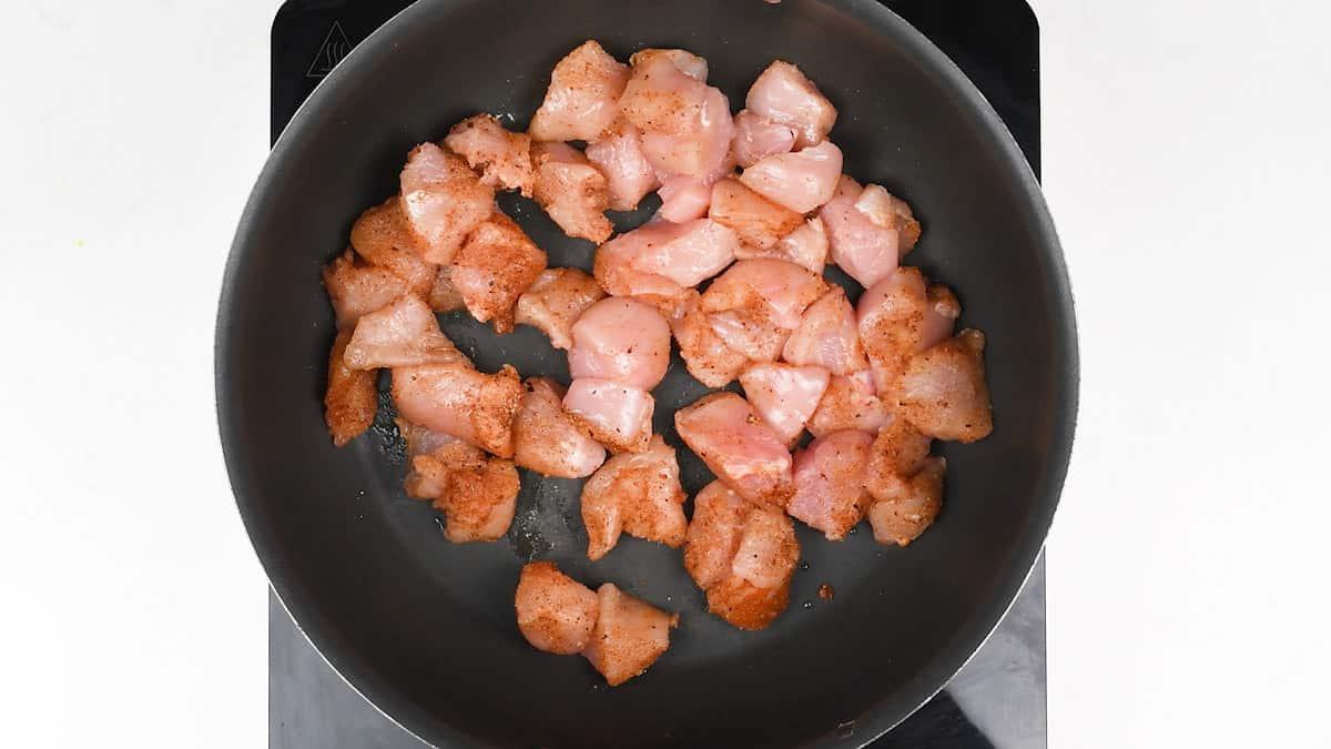 Cajun-seasoned chicken pieces browning in a large nonstick pan