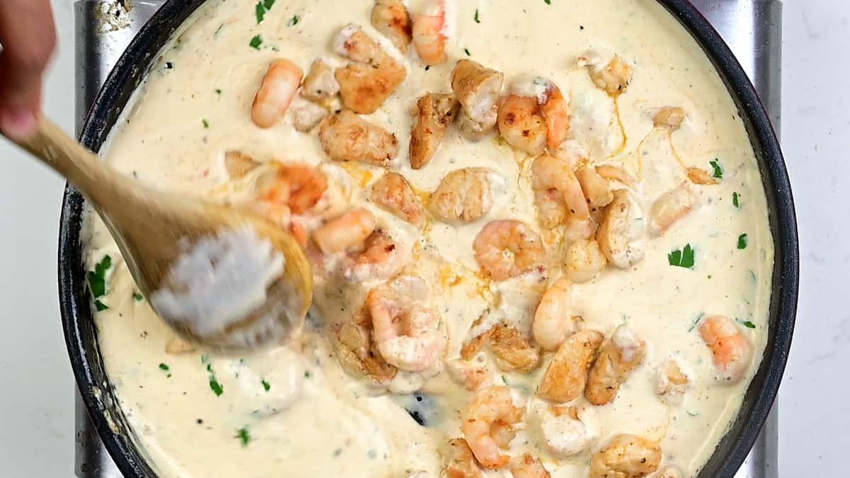 Stirring chicken and shrimp into Alfredo sauce