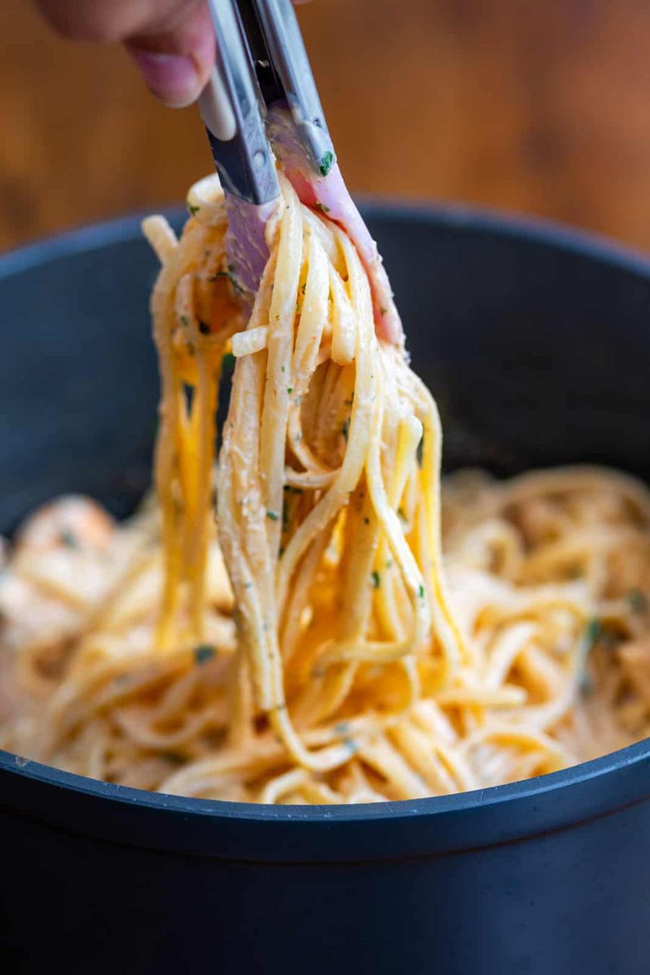 tossing pasta using tongs in a pot