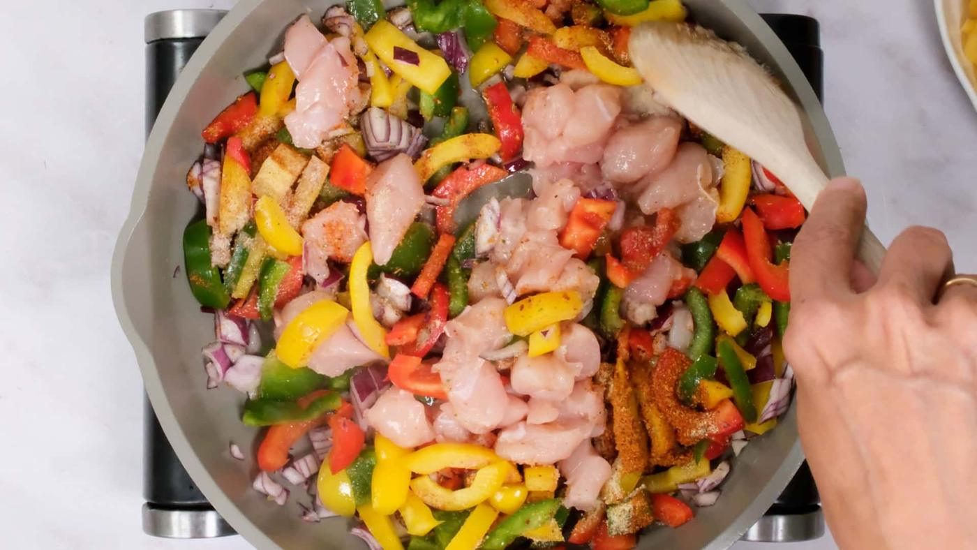 stirring chicken into pan with peppers and onion
