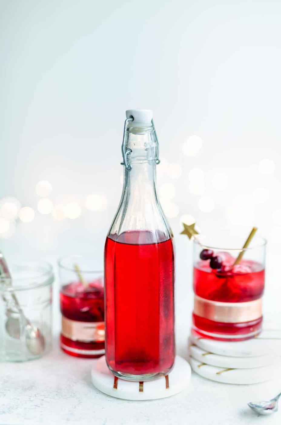Bottle of homemade cranberry infused vodka with vodka cranberry drinks on side