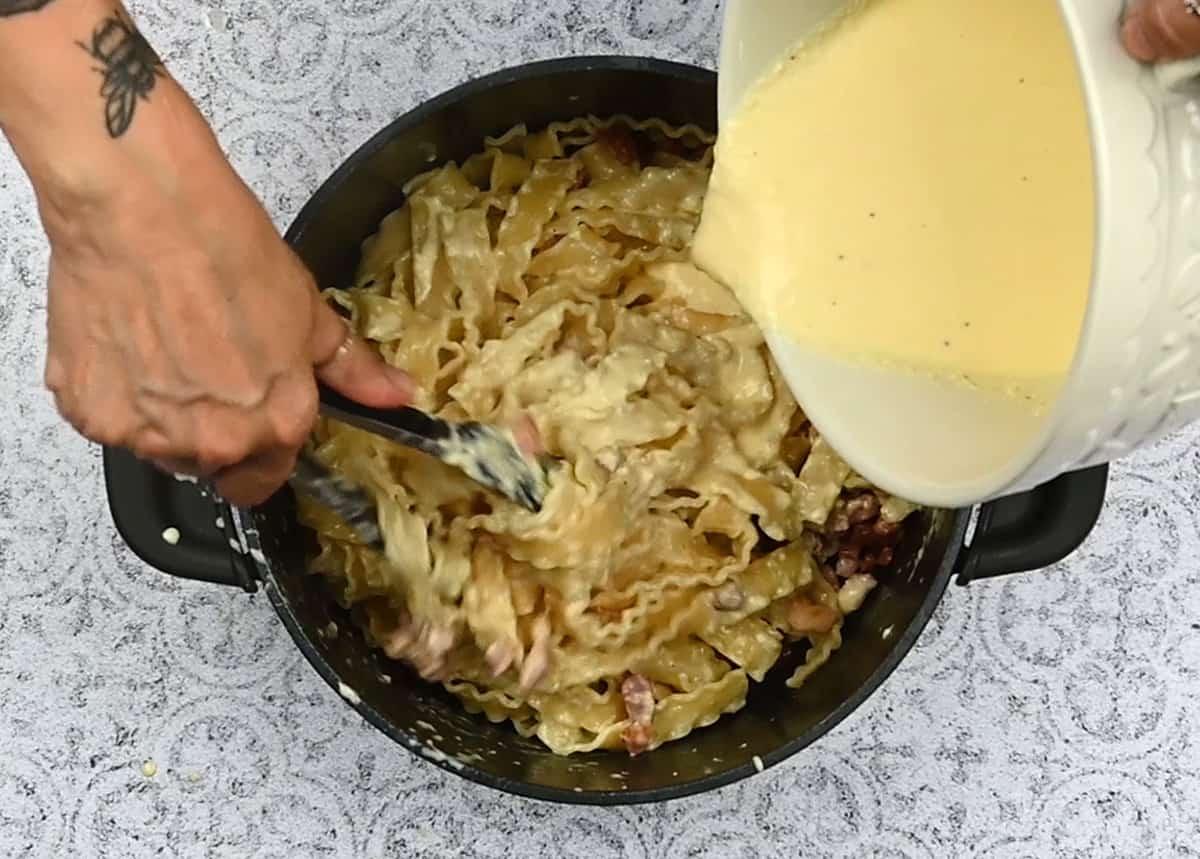 adding creamy carbonara sauce to pasta