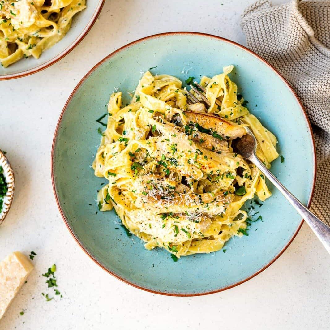 Serving of creamy chicken pasta in a blue bowl garnished with grated Parmesan and parsley (overhead view)