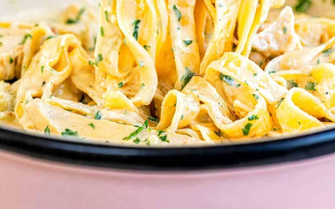 Tongs holding up creamy chicken Alfredo tagliatelle