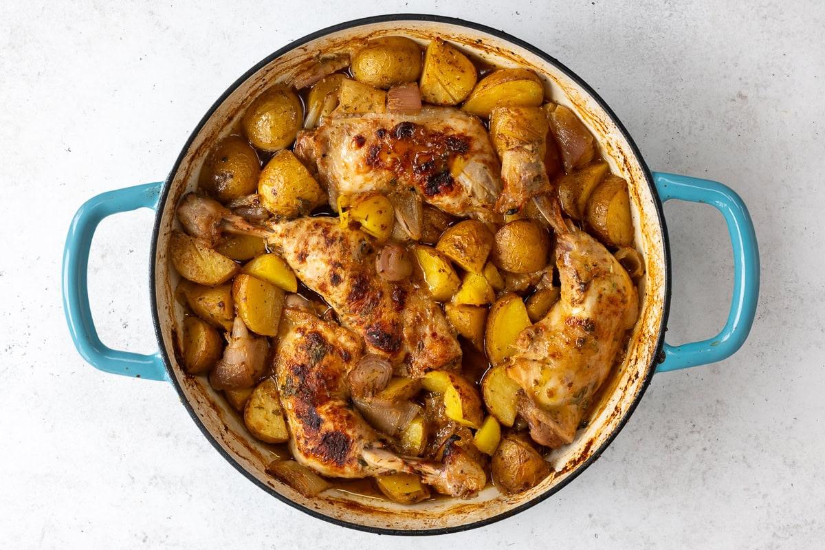 shallow cast iron casserole dish with chicken leg quarters cooked with potatoes