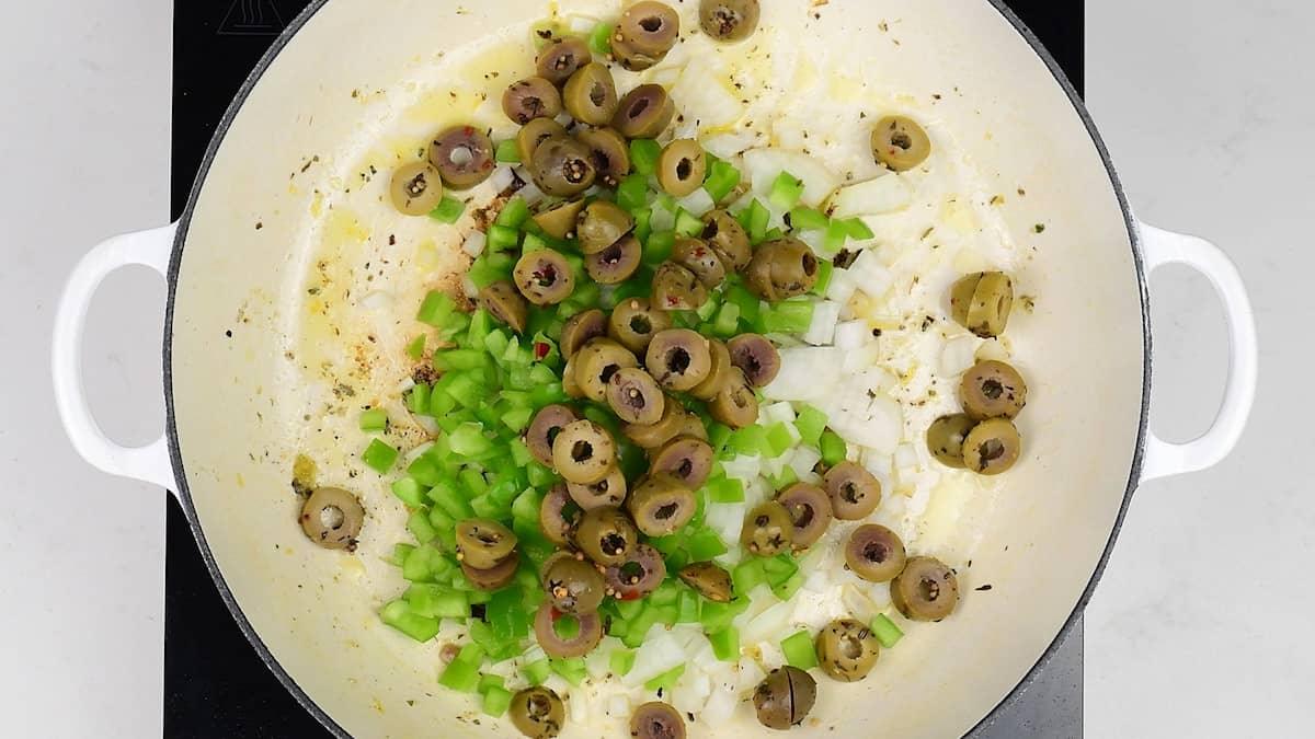 onions, green pepper and diced olives cooking in shallow cast iron pan