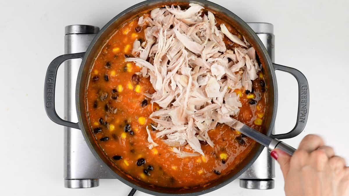 Adding shredded chicken to pot of enchilada soup