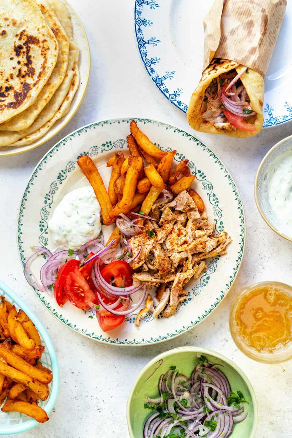 Chicken gyros on a plate with tzatziki sauce, Greek salad and fries with pita bread on the side