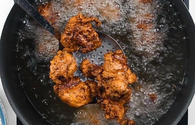 Close up of chicken frying in a large pot of oil