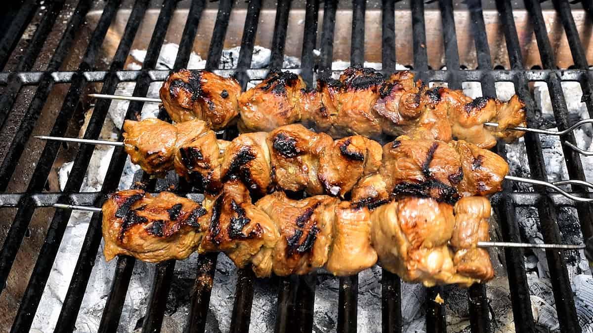 Chicken Kebabs sizzle on skewers, the marinated meat grilling over an open flame. Visible char marks and rising smoke add to the mouthwatering aroma wafting from the barbecue grill.