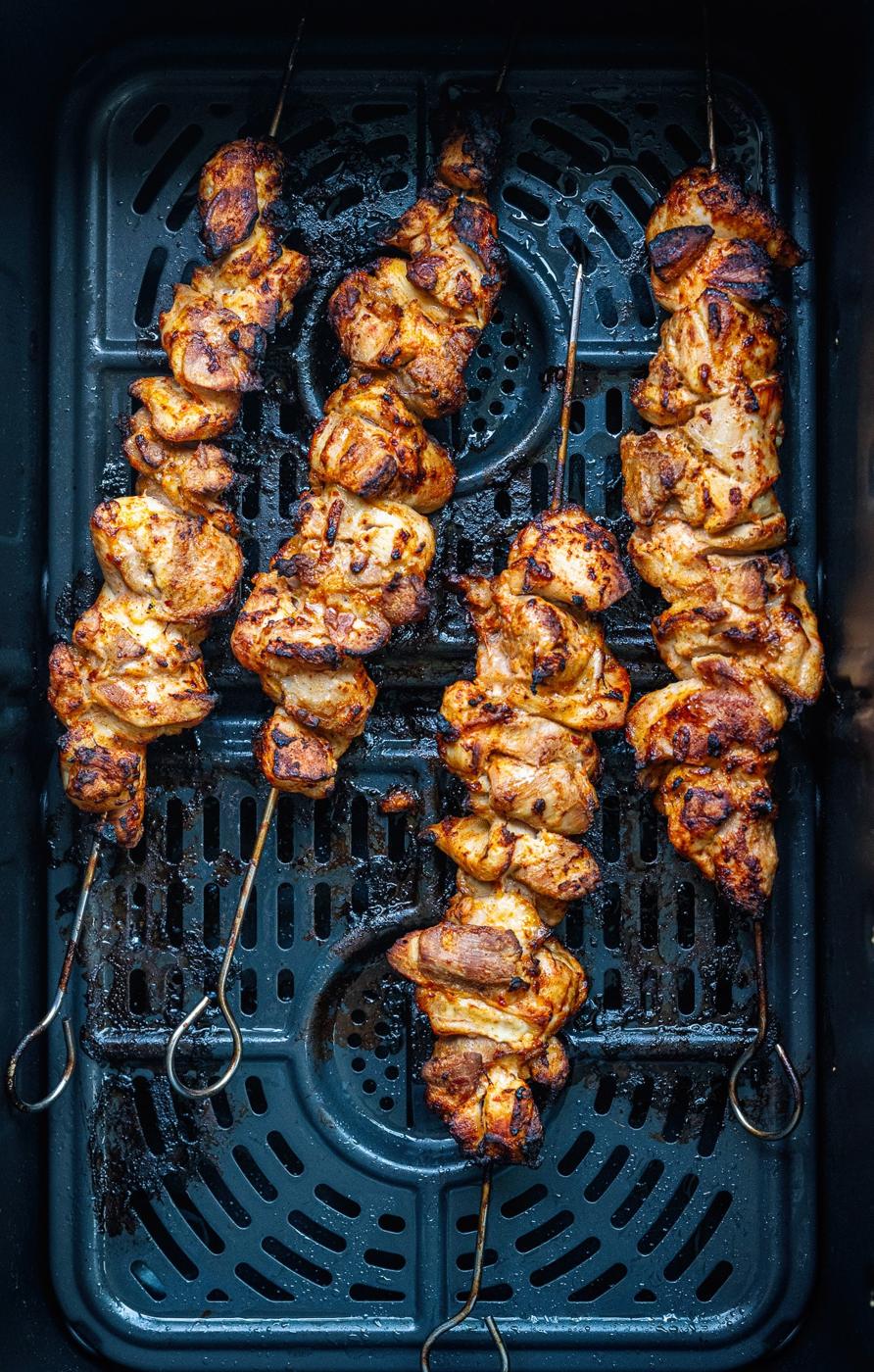 Four skewers of seasoned Chicken Kebabs are arranged in an air fryer basket. The chicken is golden brown with charred edges, indicating it has been cooked thoroughly.